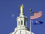 The Wisconsin statute atop the dome points toward Lake Monona as the Wisconsin state flag and U.S. flag fly above the Capitol. 