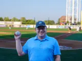 Sen. Spreitzer smiles with a baseball after throwing the first pitch at a Beloit Sky Carp game. 