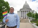 Sen. Spreitzer stands with a Progress Pride flag in front of the Capitol building. 