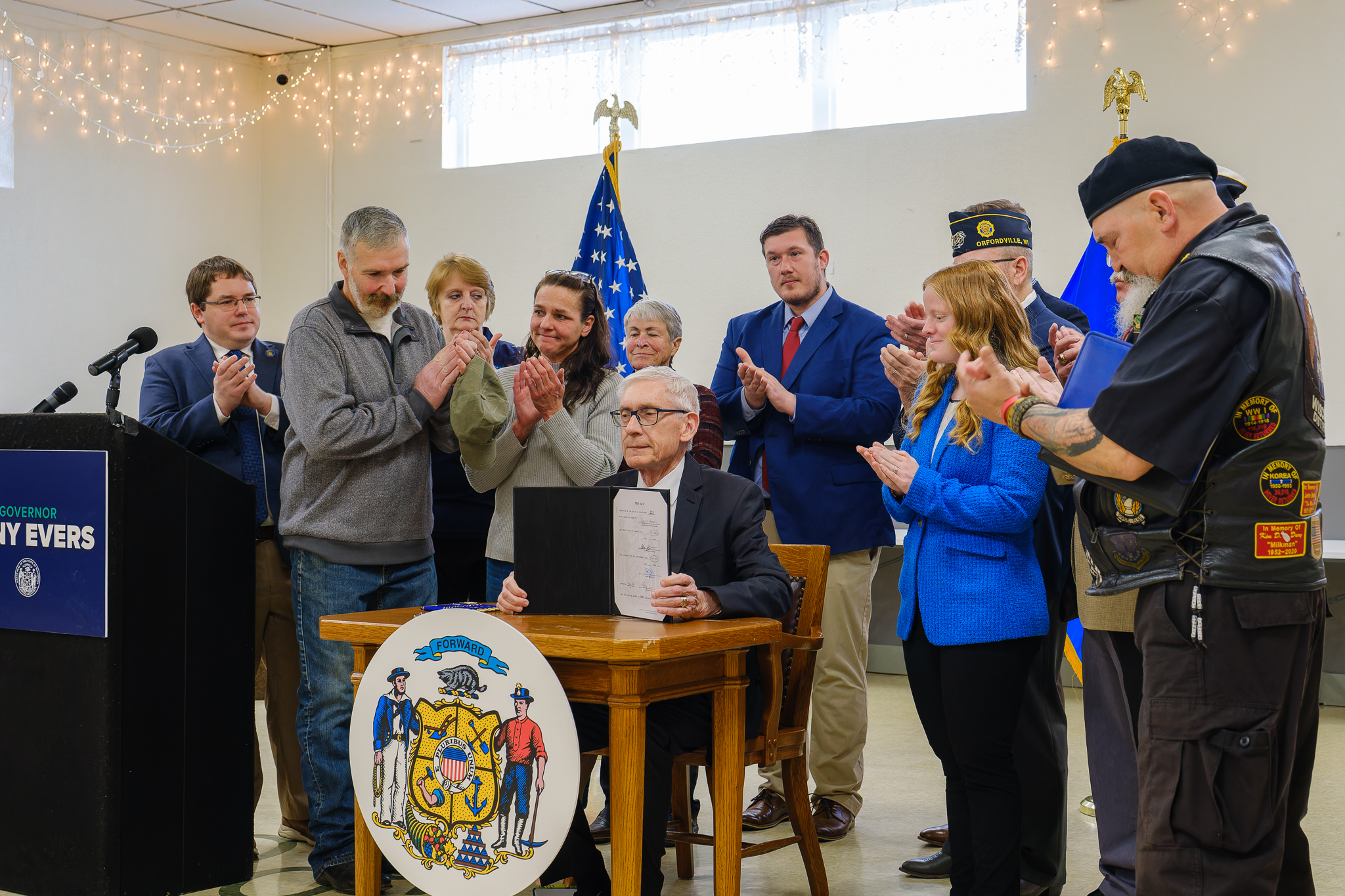 Governor Tony Evers signs 2023 Wisconsin Act 215 into state law in Orfordville while Senator Spreitzer and local leaders applaud.