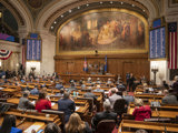 Governor Tony Evers delivers his state of the state address in the  assembly chamber. He is standing on the rostrum speaking to an audience of legislators and their guests sitting in rows before him. 