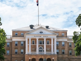 Bascom Hall on the University of Wisconsin Madison campus. The flags are flying and it's a sunny day with light clouds in the background. 