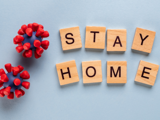 A graphic on a light blue background with scrabble tiles that spell out "stay home" alongside two cartoon red and grey COVID-19 viruses.