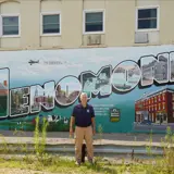 Senator Smith standing in front of the mural for the city of Menomonie.