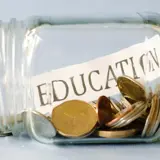 Jar on its side filled with coins and a slip of paper with education written on it.