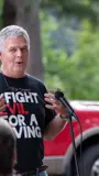 Senator Smith speaking at an event wearing I Fight Evil For A Living shirt.