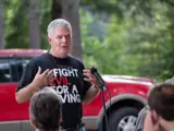 Senator Smith speaking at an event wearing I Fight Evil For A Living shirt.