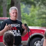 Senator Smith speaking at an event wearing I Fight Evil For A Living shirt.