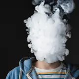 Person exhaling smoke in a large puff that covers their face.