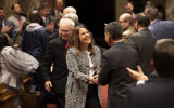 Senator Dianne Hesselbein shakes hands with someone at hte 2023 Budget Address. She is wearing a black and white patterened jacket as she smiles at the person whose hand she's shaking. Many other people are in the foreground and background, clapping and celebrating the speech.